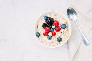 Oatmeal with raspberries, blueberries, blackberries and nuts on a gray concrete background. Healthy healthy breakfast. Flat lay