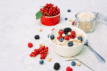 Oatmeal with raspberries, blueberries, blackberries, red currants and nuts on a gray concrete background. Healthy healthy breakfast.