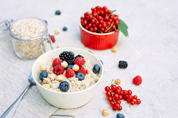 Oatmeal with raspberries, blueberries, blackberries, red currants and nuts on a gray concrete background. Healthy healthy breakfast.