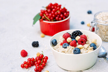 Oatmeal with raspberries, blueberries, blackberries, red currants and nuts on a gray concrete background. Healthy healthy breakfast.