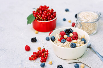 Oatmeal with raspberries, blueberries, blackberries, red currants and nuts on a gray concrete background. Healthy healthy breakfast.