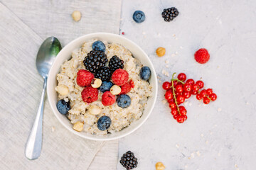 Oatmeal with raspberries, blueberries, blackberries, red currants and nuts on a gray concrete background. Healthy healthy breakfast. Flat lay