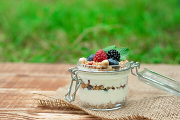Muesli granola with yogurt and fresh raspberries, blueberries and blackberries, nuts in a glass jar on a wooden background. Healthy and healthy breakfast.