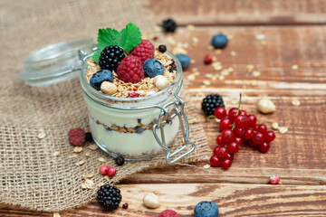 Muesli granola with yogurt and fresh red currant berries raspberries blueberries and blackberries, nuts in a glass jar on a wooden background. Healthy breakfast.