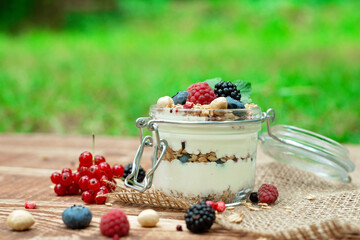 Muesli granola with yogurt and fresh red currant berries raspberries blueberries and blackberries, nuts in a glass jar on a wooden background. Healthy breakfast.