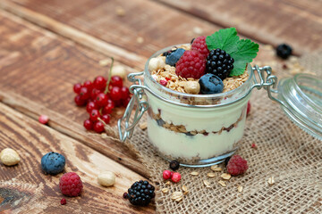 Muesli granola with yogurt and fresh red currant berries raspberries blueberries and blackberries, nuts in a glass jar on a wooden background. Healthy breakfast.