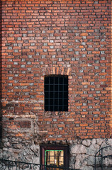 Fototapeta na wymiar Red brick wall with a vintage window with a metal grate. The concept of a prison, confinement, ancient architecture of Lviv.