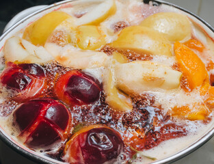Fruit compote: apricots, plums, apples, cherries are cooked in a metal pan in boiled water with bubbles. Making juice on the stove.