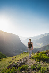 Fototapeta premium Young woman stands on the top and looks at a beautiful valley between the mountains. Backpack hiking.