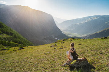 Fototapeta premium Young woman sits on the top against the background of a beautiful valley between the mountains. Backpack hiking.