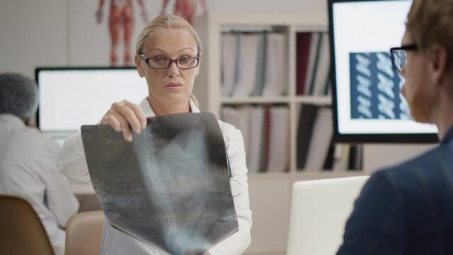 Serious female doctor pointing at x-ray image of lungs and chest consulting senior patient in clinic