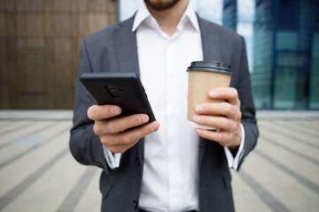 Cropped image of business man using phone and coffee cup standing near business center