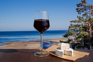Glass of red wine with brie cheese with view of the White Dune and Baltic see in spring, Latvia. Beach with white sand and blue sea/ocean. Beach with pine forest