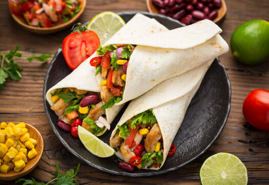 Fresh tortilla wraps with chicken meat and vegetables on the wooden table