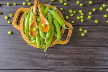 ripe sweet green peas in the pods in the bowl and wooden spoons in the top view. background with sweet pea pods close-up. sweet peas lay flat on the wooden table.