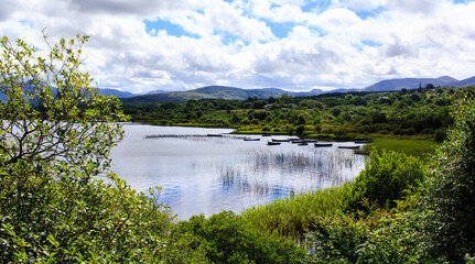 Fototapeta na wymiar Shot of the lake with boats surrounded by luxuriant greenery in Connemora, Western Ireland. 