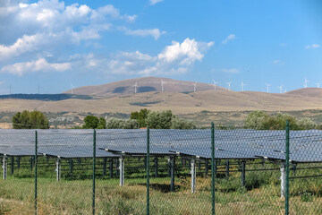 Power generation plant, with several solar panels and wind turbines in the background, commune of Pescina, Abruzzo region, province of Aquila, Italy