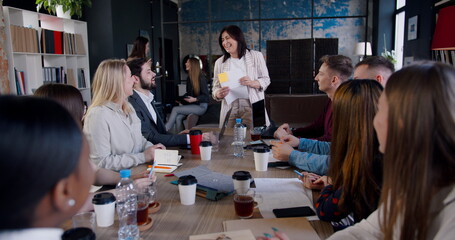 Multiethnic business people clap to successful happy middle aged brunette female coach speaking at...
