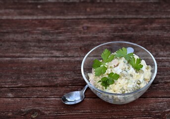 Russian salad Olivier with potatoes, chicken, eggs, cucumber, green peas in a bowl on a wooden background in rustic style copy space