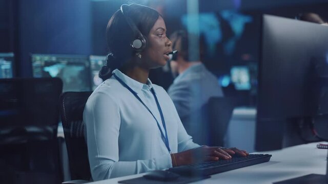 Joyful Beautiful Technical Customer Support Specialist is Talking on a Headset while Working on a Computer in a Call Center Control Room Filled with Colleagues, Display Screens and Data Servers.