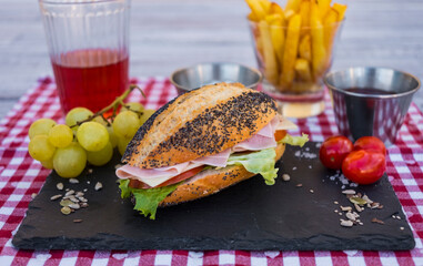 Inviting poppy seed sandwich with fresh vegetables, and ham. Light and healthy snack on a black stone cutting board