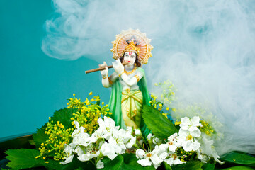 Obraz na płótnie Canvas Hindu god Krishna. Statue with flowers and smoke on a blue background.