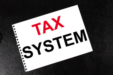 TAX SYSTEM. TEXT ON WHITE SHEET OF PAPER ON BLACK BACKGROUND