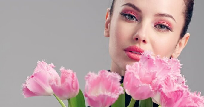 Beautiful white girl with flowers. Stunning brunette girl with big bouquet flowers of tulips. Closeup face of young beautiful woman with a healthy clean skin. Woman with bright makeup. Slow motion