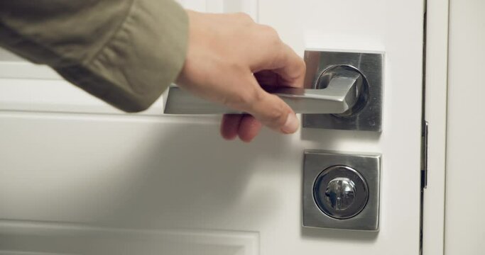 Close-up of a female hand opening a white door with a metal handle to a dark room.