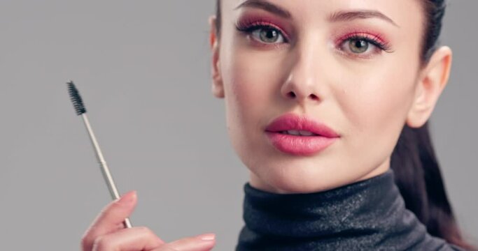 Woman makes makeup. Young woman paints her eyelashes with an eyelash brush.  Cosmetic concept. Beautiful brunette model doing make-up. Closeup view.