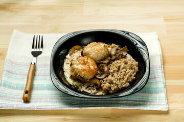 Chicken meatballs with mushrooms in a creamy sauce with green buckwheat in a black plate on a linen napkin.