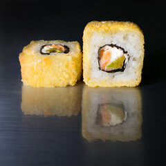 Roll of rice with avocado and salmon in nori seaweed and breading, as well as with cream cheese on a dark background with reflection