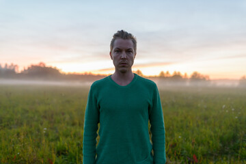 Young handsome man against grass field with fog in the break of dawn