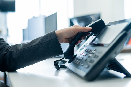 Closeup female hand on landline phone in office. Faceless woman in a suit works as a receptionist answering the phone to customer calls.