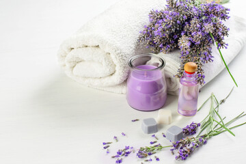 Fototapeta na wymiar Lavender flowers, soap, candle, skin oil and white towels on the white background. Spa aroma therapy, skin care.
