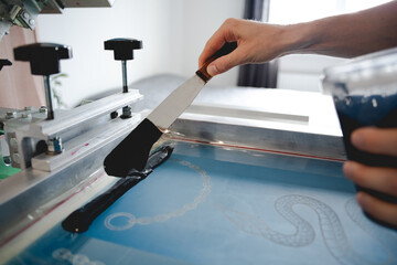 Cropped view of craftsman holding ink spatula and jar of plastisol in while working with screen...