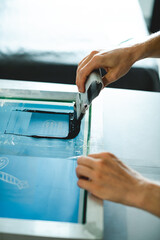 Cropped view of artisan applying plastisol ink on stencil while working with screen printing machine