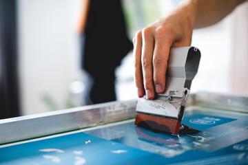 Cropped view of man holding squeegee while working with plastisol ink on screen printing machine