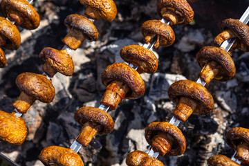Mushrooms are roasted on fire on metal skewers over charcoal. Champignons grilled on brazier. Close-up photo made during bbq .