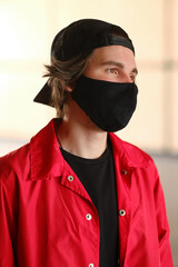 Portrait of a young man 25-30 years old in a black protective mask, black cap and red jacket. 