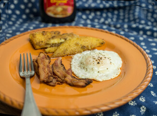 Fried slices of cornmeal polenta with bacon and a fried egg on terra-cotta colored plate. 