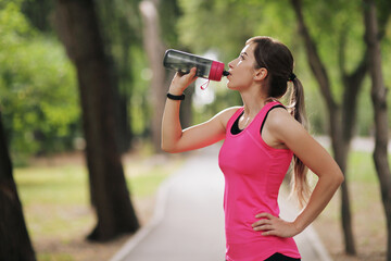 Beautiful fitness athlete runner woman drinking water in the park. Water bottle