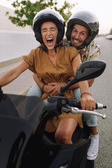 The girl rolls her boyfriend on a motorcycle. Girl is driving a motorcycle, the guy is sitting in the back.