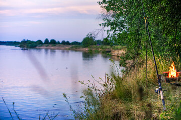 fishing rod with reel and fishing line lies on the river bank in the grass