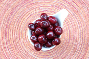 Juicy fresh cherries in a white bowl bowl agianst colorful background concentric vibrant circles in soft focus top view
