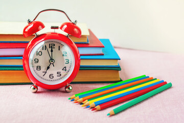 Back to school. Red alarm clock, colored pencils and stack of the book on light background, selective focus.