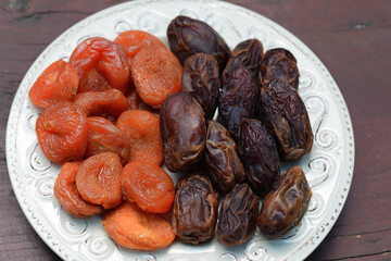 Dates and dried apricots, dried fruits on a plate on a wooden kitchen table