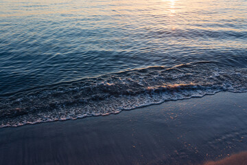 sandy beach at sunrise golden hour with calm, blue ocean and sunbeam reflection in water