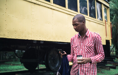 Fototapeta na wymiar A shallow focus of a young African American male in a red and white chequered shirt using his phone in a park