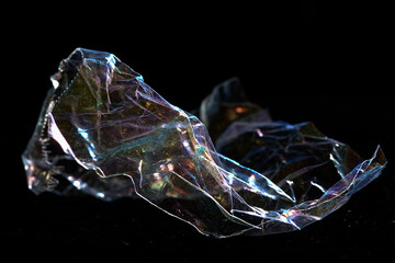 Plastic wrap - rainbow colors waste, pollution, dark background isolated